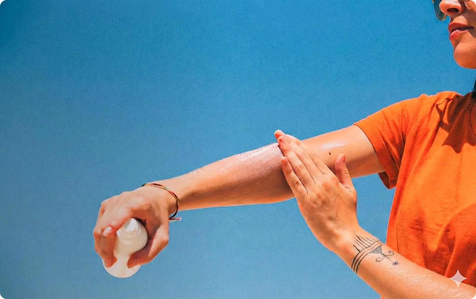 Woman applying lotion to her arm against a blue sky