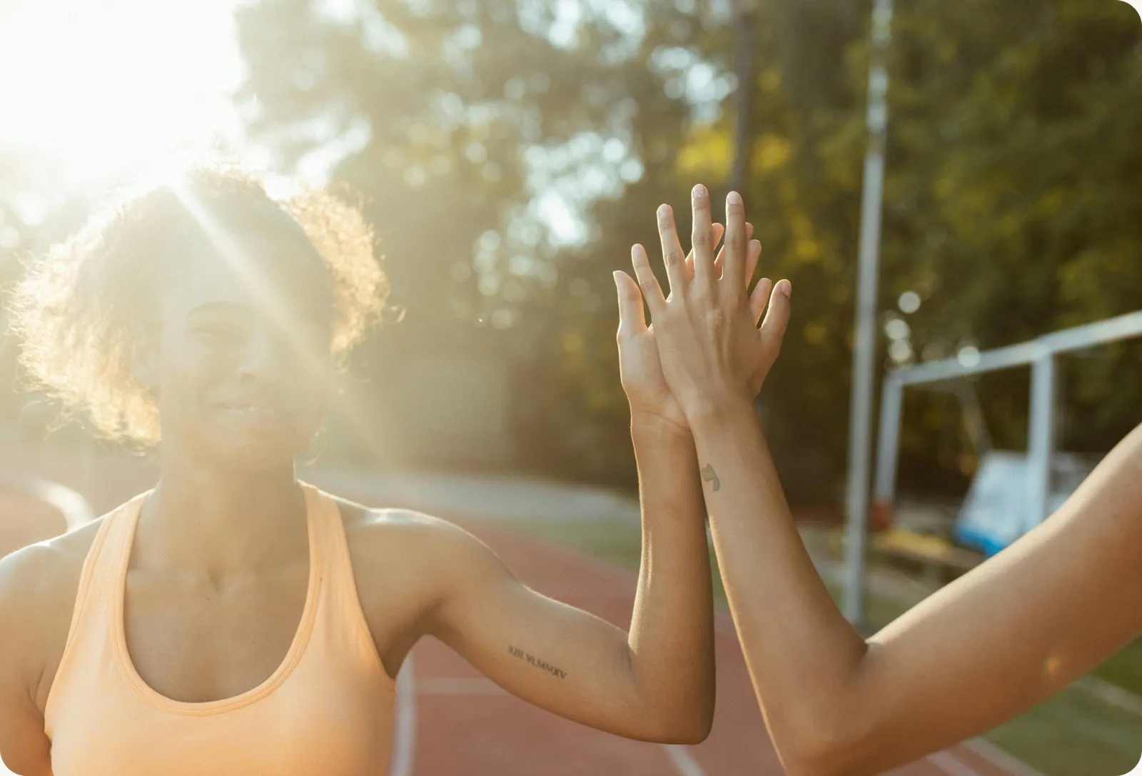 Two women high-fiving on a running track at sunset